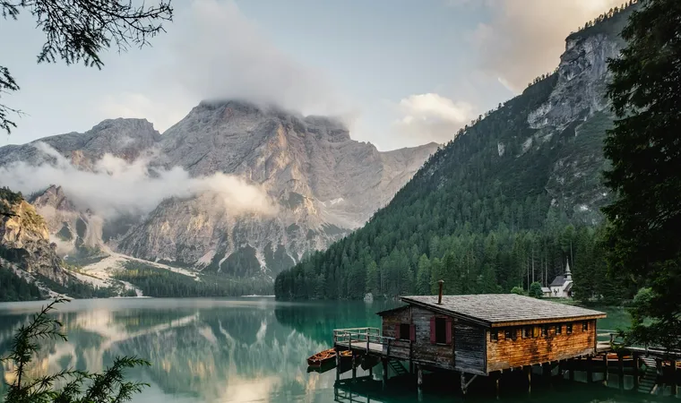 A lakeside cabin and still water beneath cloud-covered alpine mountains